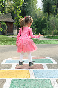 穿着粉红色连衣裙的小女孩在街上玩跳房子。