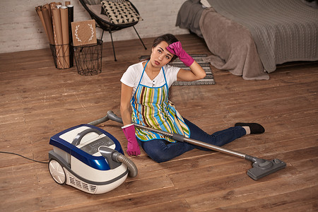坐在真空吸尘器上的一位年轻家庭主妇厌倦了家务劳动。