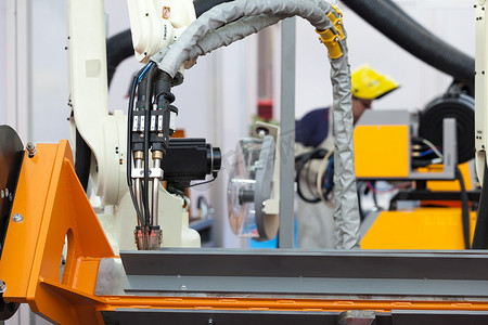 工业焊接机器人手臂处于焦点，背景中焊机模糊