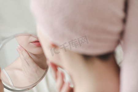 照镜子的女子摄影照片_头上戴着毛巾的年轻女子照镜子，在脸上涂抹奶油