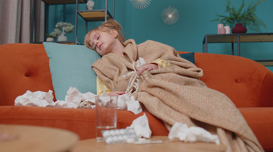 儿童高热摄影照片_患感冒发烧过敏的格子女孩，在家里沙发上把鼻涕吹进餐巾纸