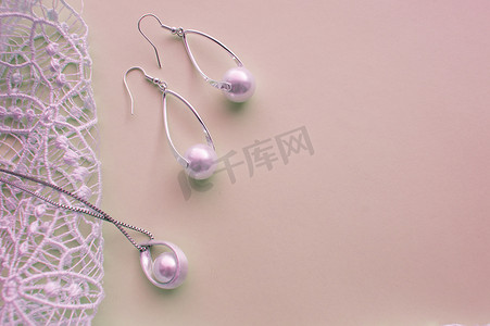 美丽的银色闪亮珍珠首饰，时尚迷人的耳环，粉色紫色背景上的链条，配有精致的蕾丝。