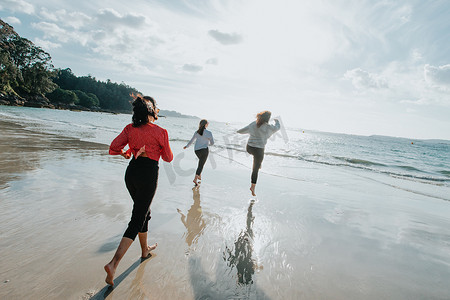 快乐的女性朋友在阳光明媚的日子里在海边跑步，朋友们快乐地放松，在傍晚日落时在海边的海滩上玩耍。
