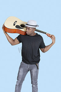 器材音乐摄影照片_浅蓝色背景中携带吉他的年轻非洲裔美国人