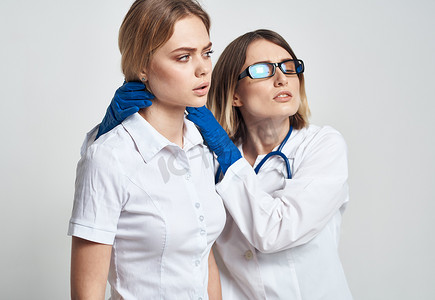 一名戴着蓝色手套的护士在浅色背景下检查一名身穿白色 T 恤的病人