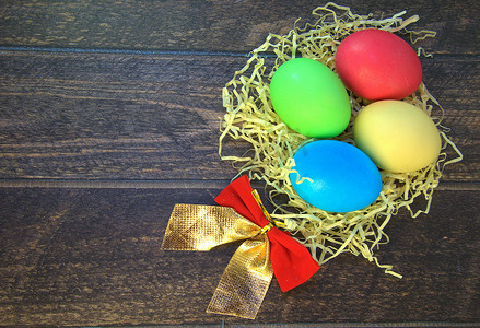 木桌上放着四个彩绘复活节彩蛋，放在一个带蝴蝶结的稻草巢里。