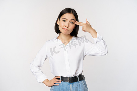 疲惫背景摄影照片_疲惫的亚洲女性的形象，对 smth 感到恼火，用手指指着她的头，站在白色背景上
