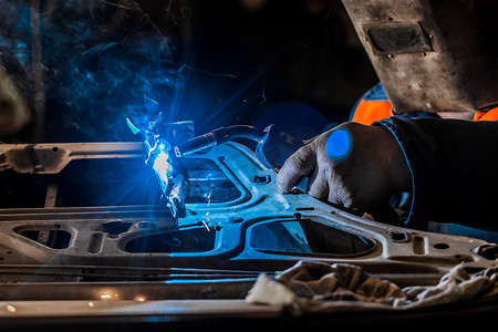 防护罩中的焊工在工业厂房的车间从事汽车门的焊接和金属、工作和修理