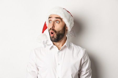 特写：戴着圣诞帽、留着胡须的惊奇男子，面带惊讶的脸向左看，圣诞促销优惠，站在白色背景上