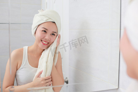 擦头发摄影照片_年轻的亚洲女人在浴室里用毛巾擦脸。