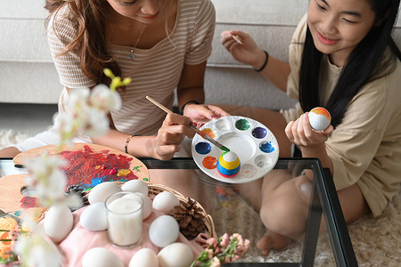 可爱摄影照片_可爱的小女孩和妈妈正在给鸡蛋上色，准备在家里一起庆祝复活节。