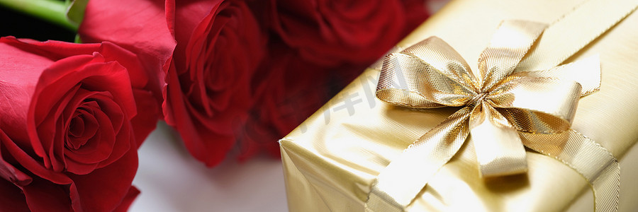 可爱装饰丝带摄影照片_红玫瑰花蕾和带丝带的金纸礼物