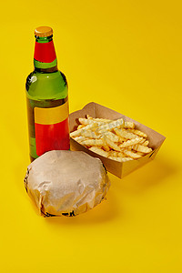纸包汉堡、纸箱薯条和黄色背景饮料瓶