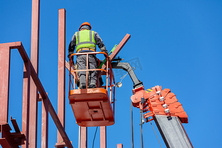 男性建筑工人在升降摇篮中高空作业，建造建筑物的铁框架