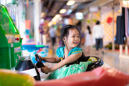 商场玩具摄影照片_穿着公主服装的亚洲小女孩在商场里乘坐玩具车