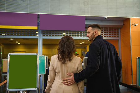 在机场航站楼等待登机、海关和护照检查时，一对年轻商业伙伴站在登机柜台的后视图。