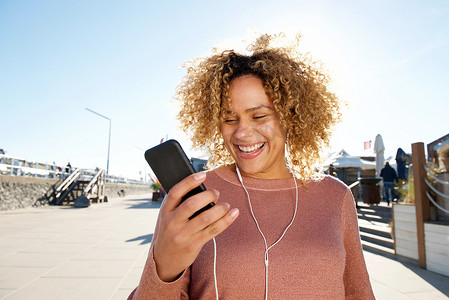快乐的非洲裔美国女人戴着耳机和手机听音乐