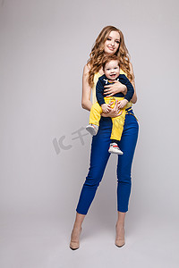 抱着小孩的母亲摄影照片_穿着休闲服的年轻健壮的女人抱着小孩。
