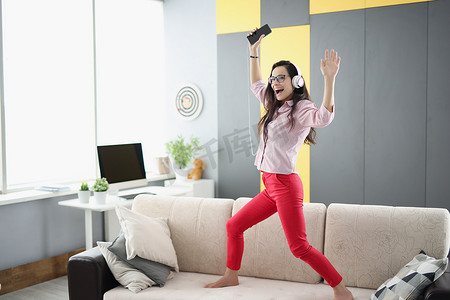 快乐的女人在沙发上跳舞，戴着耳机听音乐唱歌