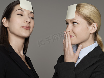 灰色背景下额头上贴着便签的两名女上班族