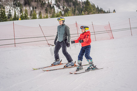 倾听和学习摄影照片_男孩在冬天在斜坡上学习滑雪、训练和听他的滑雪教练