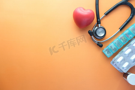 药丸形摄影照片_橙色背景中的心形符号和听诊器