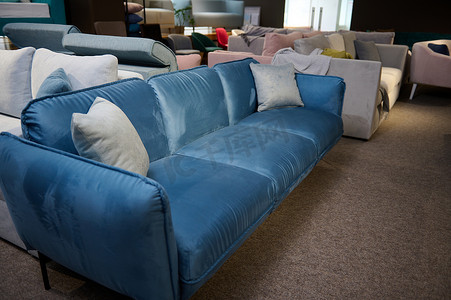 蓝色商业简约摄影照片_美丽简约时尚的蓝色丝绒沙发配有浅灰色枕头，在家具店陈列室出售。