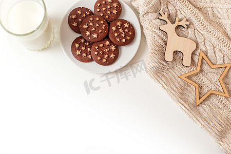 白色盘子摄影照片_在一张白色的桌子上，一个装有圆形巧克力曲奇饼的碟子，一杯牛奶