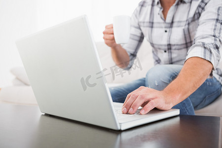 一个拿着杯子的男人使用笔记本电脑