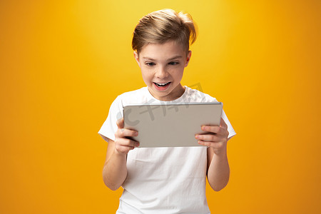 黄色背景下玩数字平板电脑的小男孩