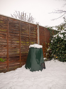 后花园绿色垃圾箱盖、栅栏和地板上的雪