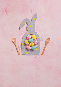 粉红色混凝土背景中兔子形框架中的彩色圆点复活节彩蛋