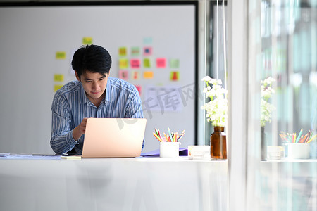 年轻的亚洲男性网络开发人员在现代工作场所从事移动应用软件设计项目。