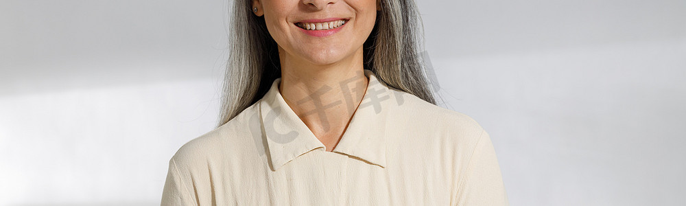 灰白的头发摄影照片_浅色背景中身穿米色衬衫、头发灰白的漂亮女人的画像