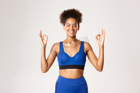 健康强壮的非洲裔美国女性运动员腰部向上，眨眼微笑，表现出好的迹象，站在白色背景上