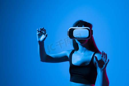 中同摄影照片_特写年轻女性站在工作室里，戴着 VR 眼镜，在虚拟空间中用手滑动滚动缩放，同时与 metaverse 中的对象交互。