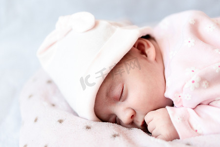 枕套摄影照片_童年、护理、母性、健康概念 — 特写小和平平静的新生女婴，戴着粉红色的帽子，睡在柔软温暖的毛毯枕套上，睡在肚子上，闭上眼睛