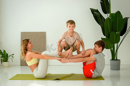 一名妇女、一名男孩和一名青少年坐在运动垫上，在他人的支持下进行集体瑜伽练习。