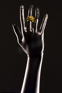 黑色背景中人体模型的黑色塑料手，手指上戴着金戒指