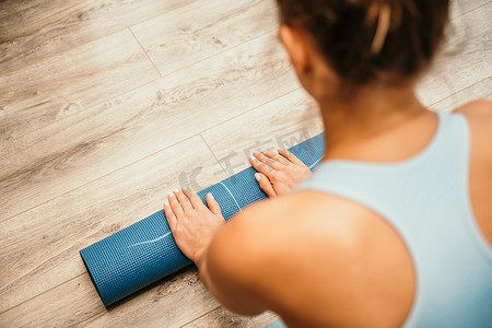 女人的手在瑜伽健身训练室的健身房地板上卷起瑜伽垫。