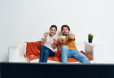 男女沙发摄影照片_看电视的年轻男女在沙发上放着爆米花和红色格子绿花