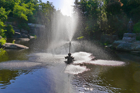 公园池塘中央的喷泉透明地溅起水花，从岸边看去，一座雕塑展现出这一切的辉煌