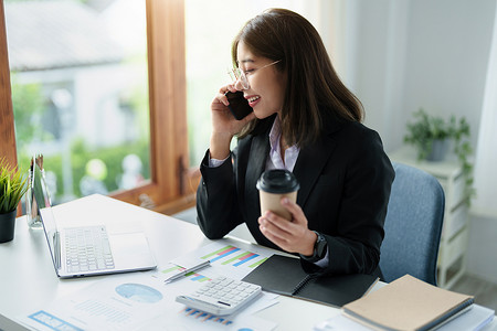 商务信函、咨询、一位亚洲女性的肖像在电话中交谈和规划财务报表和投资，并使用计算机和文件分析财务系统。