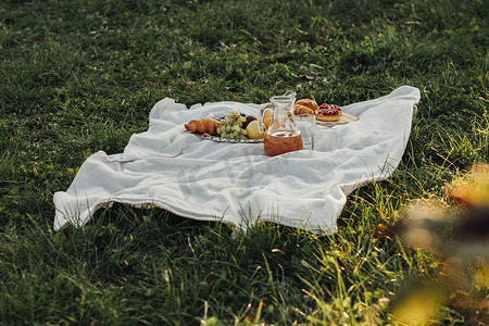日落时绿草上户外格子布上的野餐套装