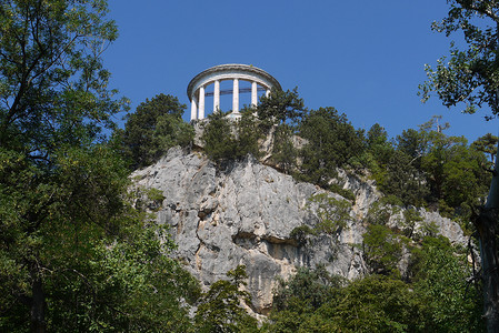 天蓝色的建筑摄影照片_岩石山顶上有一座圆形建筑，在天蓝色的背景下有白色的柱子