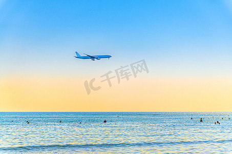 飞机在海面上低空飞行，游客在水中游泳，日落时清澈的蓝橙色天空，飞机准备降落