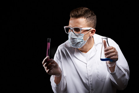戴着医用面罩的实验室助理，身穿白大衣，烧瓶中有液体，黑色背景中有化学物质