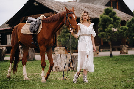 老牧场上一匹马旁边穿着白色太阳裙的漂亮女孩