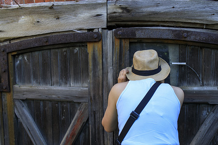 一个戴草帽的女孩从旧谷仓门缝里窥视