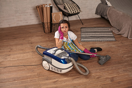 坐在真空吸尘器上的一位年轻家庭主妇厌倦了家务劳动。
